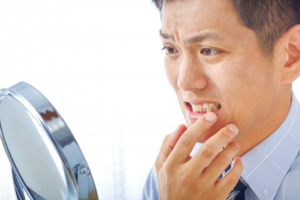 Man nervously examining his teeth in a mirror